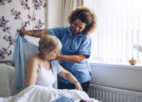 caretaker helping old lady put on robe