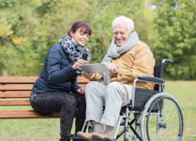 old man in wheelchair and lady using tablet