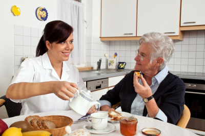 caregiver pouring milk on senior woman's tea cup